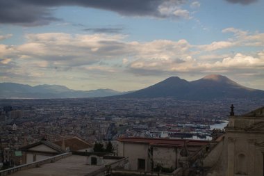 Napoli ve Napoli Körfezi 'nin güneyinde panoramik manzaralı bir şehir. Gün batımında pembe, sarı ve mavi bulutlu Vezüv volkanı. Şehir manzarası ve gökyüzü Castel Sant 'Elmo, Napoli' den.