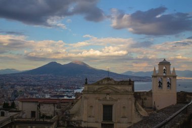 Napoli ve Napoli Körfezi 'nin güneyinde panoramik manzaralı bir şehir. Gün batımında pembe, sarı ve mavi bulutlu Vezüv volkanı. Şehir manzarası ve gökyüzü Castel Sant 'Elmo, Napoli' den.