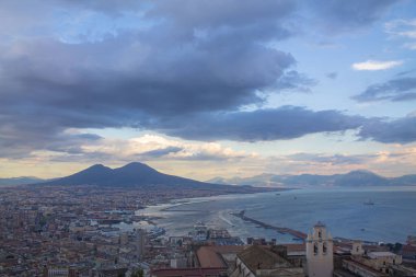 Napoli ve Napoli Körfezi 'nin güneyinde panoramik manzaralı bir şehir. Gün batımında pembe, sarı ve mavi bulutlu Vezüv volkanı. Şehir manzarası ve gökyüzü Castel Sant 'Elmo, Napoli' den.