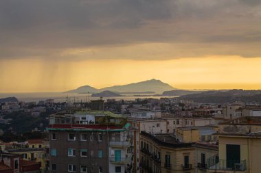 Napoli ve Napoli Körfezi 'nin güneyinde panoramik manzaralı bir şehir. Gün batımında pembe, sarı ve mavi bulutlu Vezüv volkanı. Şehir manzarası ve gökyüzü Castel Sant 'Elmo, Napoli' den.