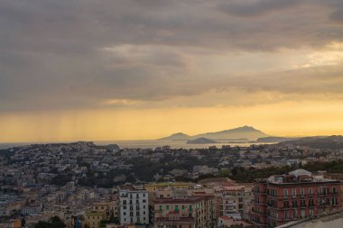 Napoli ve Napoli Körfezi 'nin güneyinde panoramik manzaralı bir şehir. Gün batımında pembe, sarı ve mavi bulutlu Vezüv volkanı. Şehir manzarası ve gökyüzü Castel Sant 'Elmo, Napoli' den.