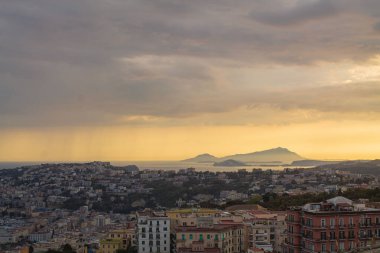 Napoli ve Napoli Körfezi 'nin güneyinde panoramik manzaralı bir şehir. Gün batımında pembe, sarı ve mavi bulutlu Vezüv volkanı. Şehir manzarası ve gökyüzü Castel Sant 'Elmo, Napoli' den.