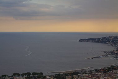 İtalya 'da körfez ve denizin üzerinde sarı gün batımı, yukarıdan manzara. Günbatımında Napoli Körfezi, panoramik manzara, İtalyan turist şehirde yürüyor ve denizde yüzen küçük tekne