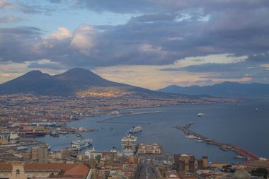 Napoli ve Napoli Körfezi 'nin güneyinde panoramik manzaralı bir şehir. Gün batımında pembe, sarı ve mavi bulutlu Vezüv volkanı. Şehir manzarası ve gökyüzü Castel Sant 'Elmo, Napoli' den.