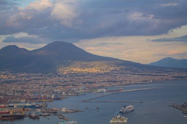 Napoli ve Napoli Körfezi 'nin güneyinde panoramik manzaralı bir şehir. Gün batımında pembe, sarı ve mavi bulutlu Vezüv volkanı. Şehir manzarası ve gökyüzü Castel Sant 'Elmo, Napoli' den.