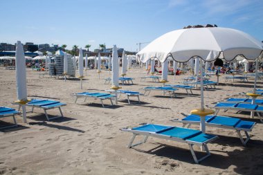 Plaj sandalyeleri ve şemsiyeler. Deniz kenarında güneşli bir günde İtalya 'da bir plajda güneşlenirler.