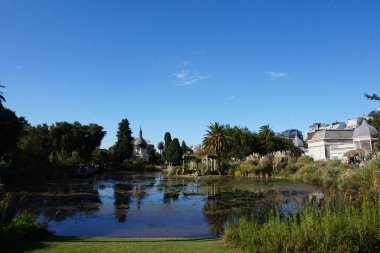 Buenos Aires Parkı 'nda park mimarisi ve mavi gökyüzü olan gölet ve yeşil ağaçların doğa fotoğrafı. Web sitesi seyahat rehberi turizmi ve tatil materyali için yansımalı manzara mükemmeldir.