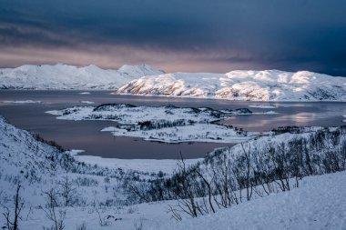 Tromso 'nun kıyı şeridinde gün batımında karlı doğa manzarası