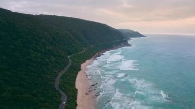 Batı Avustralya, Esperance 'da güzel bir plajın yanında çarpıcı uzun bir yol boyunca giden bir karavanın 4K insansız hava aracı videosu. Mavi okyanustan gelen beyaz dalgalar beyaz kumsala çarpıyor.