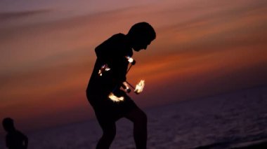 Ateş gösterisi. Sanatçılar çeşitli yangın tesislerinde çalışırlar. Erkekler ve kızlar gece plajda gün batımında ateşle dans ettiler..