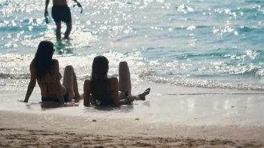 Seksi kırmızı mayo ve hasır şapkalı mutlu kadın büyüleyici okyanus sahilinde oturuyor. Kız, turkuvaz su dalgaları, beyaz kum ve güneşli tropik cennet adasındaki deniz manzarasına hayran.