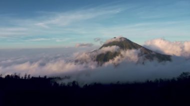 High mountain ranges with autumn brown meadows below covered with mist cloud. Coniferous trees lit by sunlight and surrounded by high mountain rocky cliffs.