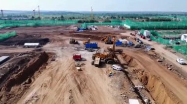 Çeşitli inşaat malzemeleri ve kamyonlarla dolu hareketli bir inşaat alanı.