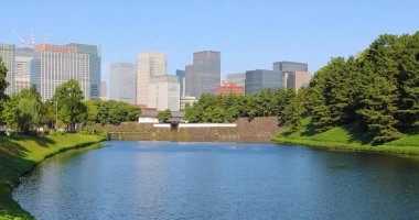 Japonya, Tokyo 'daki İmparatorluk Sarayı' nın panoramik manzarası. Ön planda, saray duvarlarını çevreleyen bir hendek var ve yemyeşil ağaçlar kıyıları sarıyor.. 