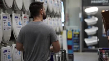Genç adam, banyo aksesuarları bölümündeki ev geliştirme hırdavat dükkanında alışveriş arabası itiyor..
