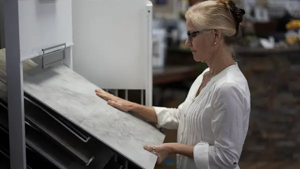 stock image Happy mature woman running hand across touching luxury vinyl tile samples in a floor store for a home remodeling project.