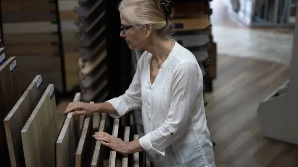 stock image Happy mature woman running hand across solid or engineered solid wood plank samples in a floor or hardware store for a home remodeling renovation project.