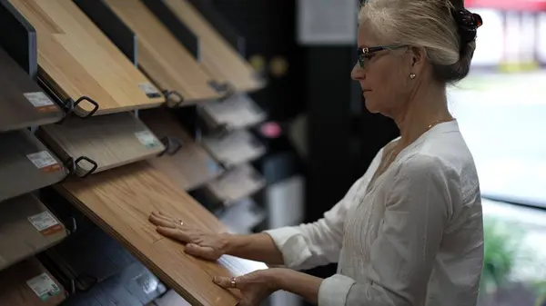 stock image Happy mature woman running hand across solid or engineered wood plank samples in a floor or hardware store for a home remodeling renovation redecorating project.