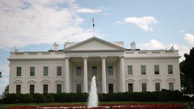 Beyaz Saray 'ın kuzey tarafına bakan, üzerinde bulutlar ve çeşmeler olan mavi gökyüzü, baharda yeşil çimenler, ağaçlar ve bayraklar dalgalanır..