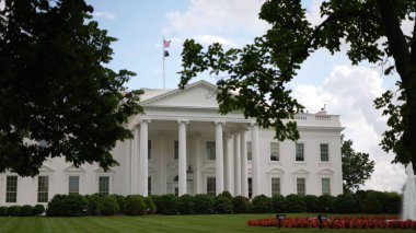 Beyaz Saray 'ın kuzey tarafındaki ağaçların arasından bak. Çeşme, yeşil çimen ve baharda dalgalanan bayraklar..