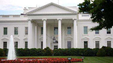 Beyaz Saray 'ın kuzeyini yakından gören, üzerinde bulutlar ve çeşmeler olan mavi gökyüzü, baharda yeşil çimenler, ağaçlar ve bayraklar dalgalanan,.