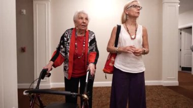 Yürüyen yaşlı bir kadın ve olgun bir bayan koridorda dikilip konuşuyor..