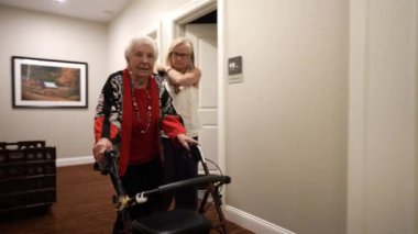 Yaşlı kadın ya da büyükanne Walker 'ı kızıyla birlikte huzurevinin koridorunda yürümek için kullanıyor..