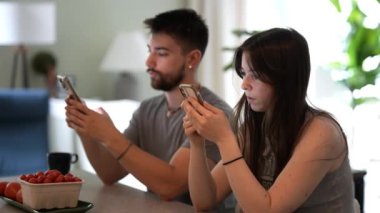 Genç çiftin telefonlarıyla ilgili bilgi paylaşıp evlerindeki bir gişede konuşup mesajlaşmaları. Kamera sola hareket ediyor..