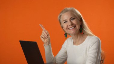 40 'lı yaşlarda olgun bir kadının turuncu arka plan stüdyosunda yalnız poz vermesine şaşırdım. İnsanların yaşam tarzı konsepti. Gözleri gören kameraya bakıyorum..