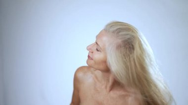 Mutlu gülümseyen 50 'li yaşlarda, 60' lı yaşlarda orta yaşlı, beyaz arka planda kameraya bakan olgun bir kadın. Yaş karşıtlığı güzellik, cilt ve vücut bakımı, sağlık ve kendine bakım kavramlarıyla yüzleşir. Portreyi kapat.