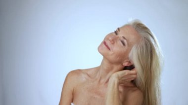 Mutlu gülümseyen 50 'li yaşlarda, 60' lı yaşlarda orta yaşlı, beyaz arka planda kameraya bakan olgun bir kadın. Yaş karşıtlığı güzellik, cilt ve vücut bakımı, sağlık ve kendine bakım kavramlarıyla yüzleşir. Portreyi kapat.