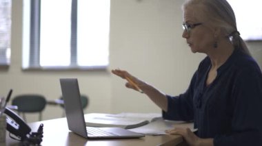 Lise matematik öğretmeni masada oturmuş öğrenciler için ödevler hazırlıyor. Yukarı bakıyor ve gülümsüyor..