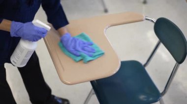 Öğretmen, 19 numaralı karantina ve tecrit sonrası okulda masaları dezenfekte ediyor..