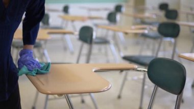 Öğretmen, 19 numaralı karantina ve tecrit sonrası okulda masaları dezenfekte ediyor..