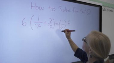 Etkileşimli bir beyaz tahtaya yazı yazan kadın öğretmenin sınıfta matematik öğrettiği yakın plan..