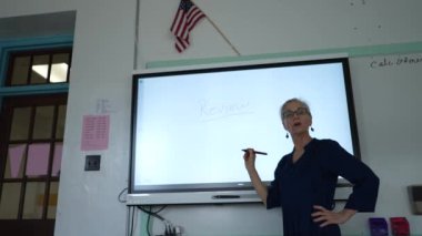 Etkileşimli bir beyaz tahtaya yazı yazan kadın öğretmenin sınıfta matematik öğrettiği yakın plan..