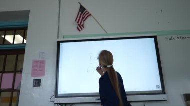 Etkileşimli bir beyaz tahtaya yazı yazan kadın öğretmenin sınıfta matematik öğrettiği yakın plan..