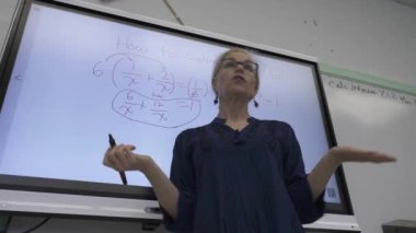 Etkileşimli bir beyaz tahtaya yazı yazan kadın öğretmenin sınıfta matematik öğrettiği yakın plan..