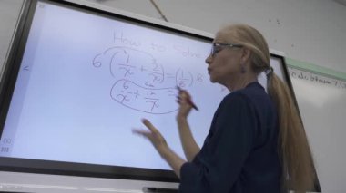 Etkileşimli bir beyaz tahtaya yazı yazan kadın öğretmenin sınıfta matematik öğrettiği yakın plan..