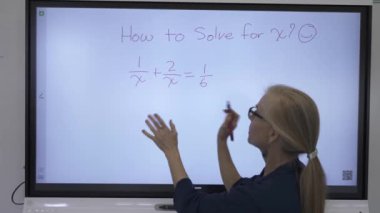 Etkileşimli bir beyaz tahtaya yazı yazan kadın öğretmenin sınıfta matematik öğrettiği yakın plan..