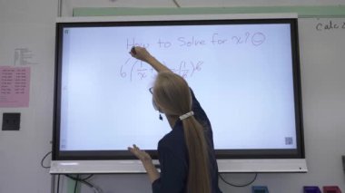 Etkileşimli bir beyaz tahtaya yazı yazan kadın öğretmenin sınıfta matematik öğrettiği yakın plan..