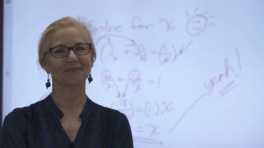 Etkileşimli bir beyaz tahtaya yazı yazan kadın öğretmenin sınıfta matematik öğrettiği yakın plan..