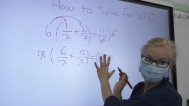 Etkileşimli bir beyaz tahtaya yazı yazan kadın öğretmenin sınıfta matematik öğrettiği yakın plan..