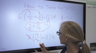 Etkileşimli bir beyaz tahtaya yazı yazan kadın öğretmenin sınıfta matematik öğrettiği yakın plan..