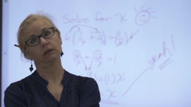 Etkileşimli bir beyaz tahtaya yazı yazan kadın öğretmenin sınıfta matematik öğrettiği yakın plan..