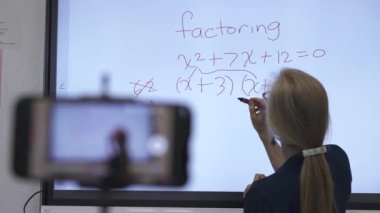 Etkileşimli bir beyaz tahtaya yazı yazan kadın öğretmenin sınıfta matematik öğrettiği yakın plan..