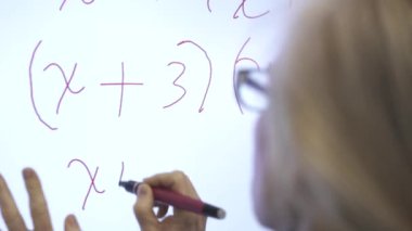 Etkileşimli bir beyaz tahtaya yazı yazan kadın öğretmenin sınıfta matematik öğrettiği yakın plan..