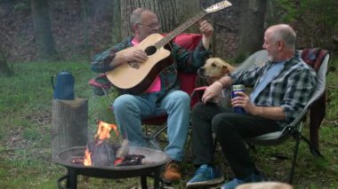 Ormanda kamp ateşinin önünde gitarlı ve köpekli iki eşcinsel aşk için kafalarını sandalyelere sürtüyor..