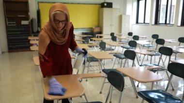 Mutlu Müslüman kadın öğretmen başörtüsü takıyor beyaz tahtaya dünya dinleri yazıyor. Sınıfta Amerikan bayrağı ve arka planda akıllı tahta var..