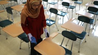 Mutlu Müslüman kadın öğretmen başörtüsü takıyor beyaz tahtaya dünya dinleri yazıyor. Sınıfta Amerikan bayrağı ve arka planda akıllı tahta var..